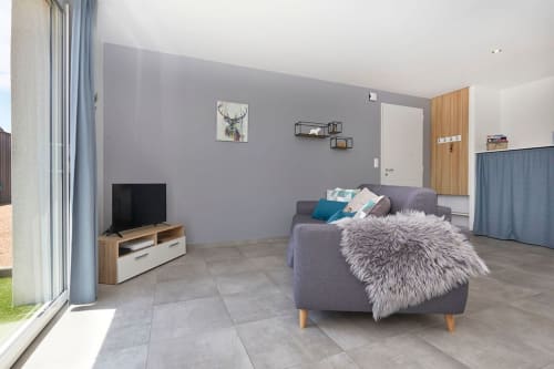 Modern living room in Appartement 2-Toronto at Résidence des Sables, Mably, with gray sofa, wooden TV stand, and purple