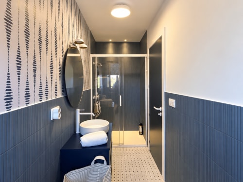 Baño moderno con azulejos azul marino, lavamanos redondo y ducha abierta en la casita El Román de Baiona con vistas al mar