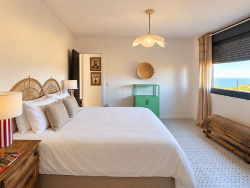 Luminoso dormitorio costero en la casita El Román, Baiona, con vistas al mar, cabecero de mimbre, armario verde y luz natural