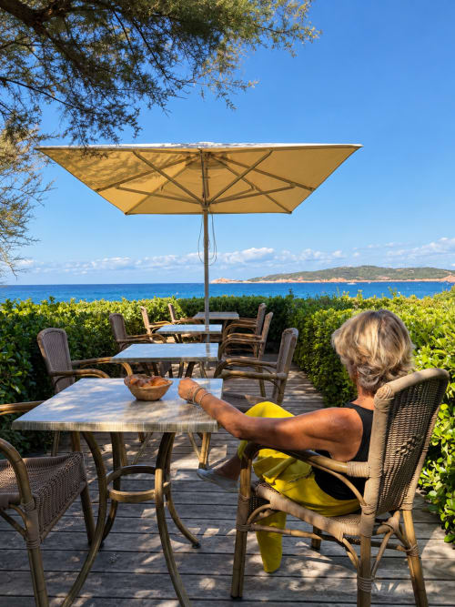 Femme se relaxant à la terrasse face à la mer de l'Hôtel Thalassa à Cargèse, parasol jaune