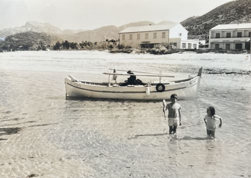 Des enfants barbotant dans les eaux méditerranéennes près d'un bateau de pêche amarré à la plage de l'Hôtel Thalassa, Cargèse
