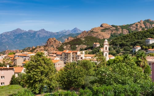 Village de Cargèse aux toits en terre cuite, clocher d'église et montagnes de granit dramatiques sous un ciel bleu