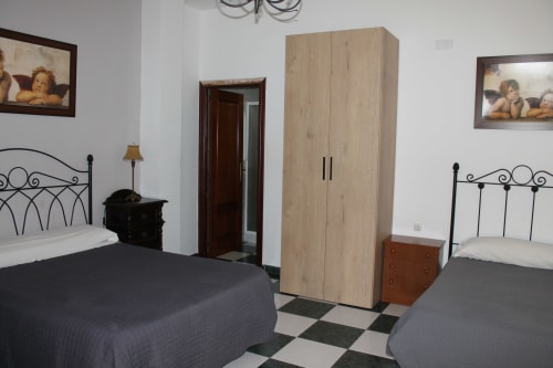 Dormitorio doble de Hostal El Camionero con camas ornamentadas, armario de madera y piso a cuadros en Burguillos del Cerro