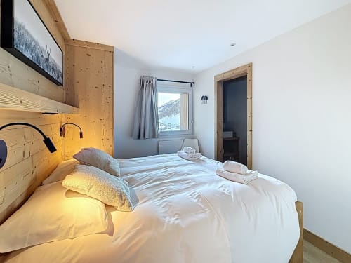 Chambre lumineuse avec mur d'accent en bois, draps blancs, coussins jaunes et vue sur les montagnes aux Tanières de Montgenèvre