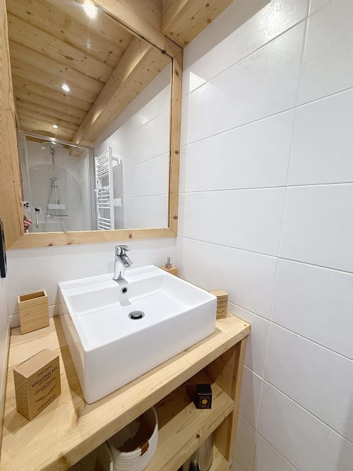 Salle de bain moderne de l'appartement Les Tanières avec vasque blanche sur vanité en bois, miroir et plafond à poutres apparentes