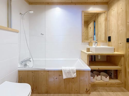 Salle de bain moderne aux finitions bois, carrelage blanc, baignoire et douche de l'appartement Les Tanières de Montgenèvre