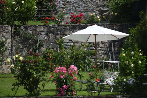 Giardino fiorito a Roseto del Drago con ombrello bianco, muri in pietra e fiori colorati a Ponte in Valtellina