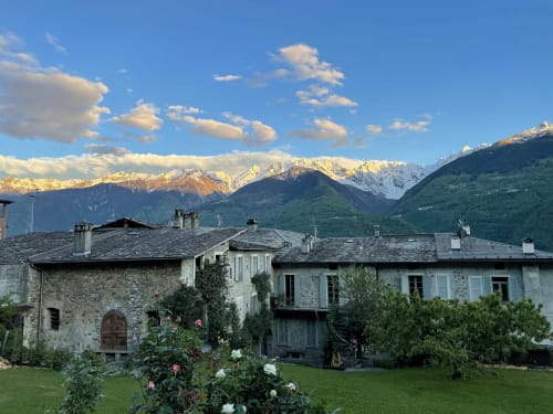 Villa in pietra a Ponte in Valtellina con le Alpi innevate sullo sfondo, giardino fiorito in primo piano, vallate verdi