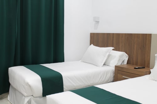 Habitación moderna de Hostal El Camionero en Burguillos del Cerro con camas gemelas, detalles verdes y cabecero de madera.