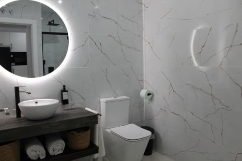Baño moderno en Hostal El Camionero en Burguillos del Cerro con azulejos efecto mármol, espejo redondo iluminado y lavamanos