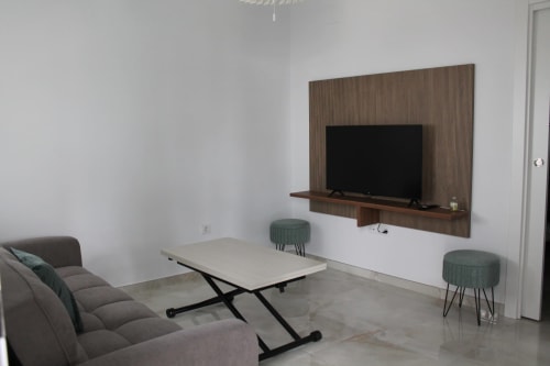 Sala moderna del Hostal El Camionero con sofá gris, TV en pared, mesa de centro y otomanas verde azulado