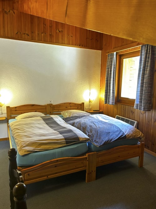 Chambre twin à l'Hôtel les Bouquetins à Zinal avec lit en bois, draps bleus et éclairage chaleureux
