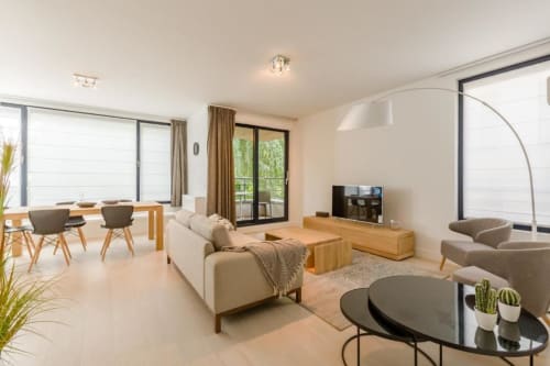 Élégant appartement ouvert The Livorno Bruxelles avec canapé crème, meubles en bois, télévision et mobilier moderne
