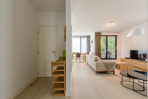 Appartement moderne à Bruxelles avec espace de vie ouvert, mobilier en bois, canapé beige et baies vitrées