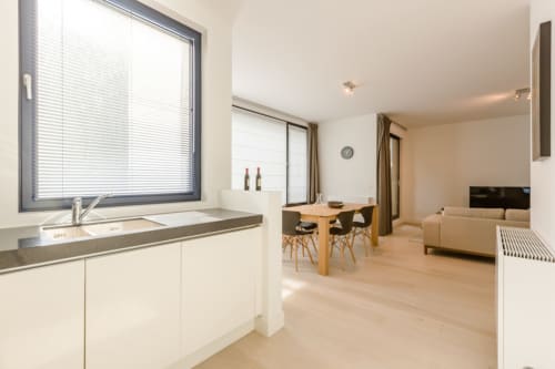 Appartement moderne et élégant à Bruxelles avec cuisine ouverte, salle à manger dotée d'une table en bois, et salon aux tons beige