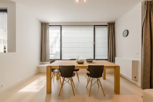 Élégante salle à manger de l'hôtel Livorno à Bruxelles avec table en bois, chaises noires et grandes fenêtres panoramiques