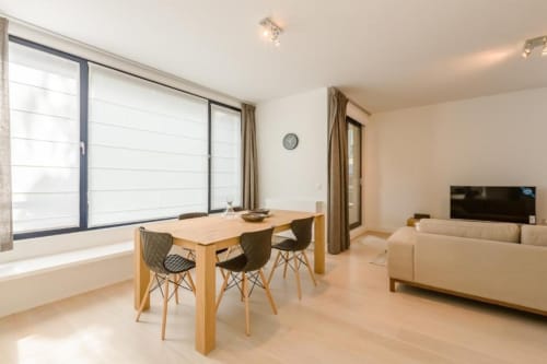 Appartement moderne à Bruxelles avec table à manger en bois, chaises noires, canapé crème et baies vitrées panoramiques au Livorno