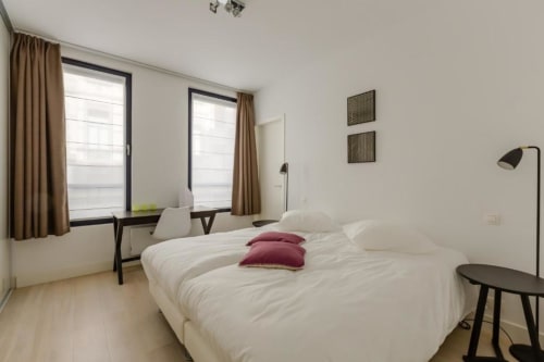 Chambre moderne élégante au Livorno Brussels avec linge blanc, oreillers bordeaux, doubles bureaux et lumière naturelle