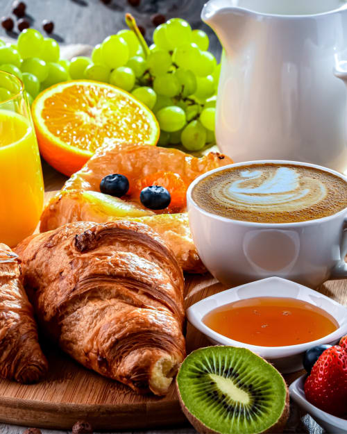 Colazione al Il Giardino di Ulisse B&B: cornetto, caffè, frutta fresca, succo e miele su tavolo in legno