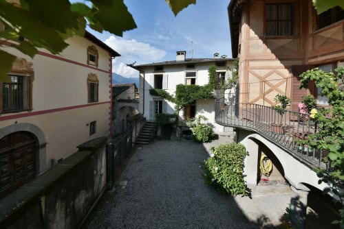 Affascinante corte interna a Roseto del Drago a Ponte in Valtellina con edifici storici in pietra e muri ricoperti di edera