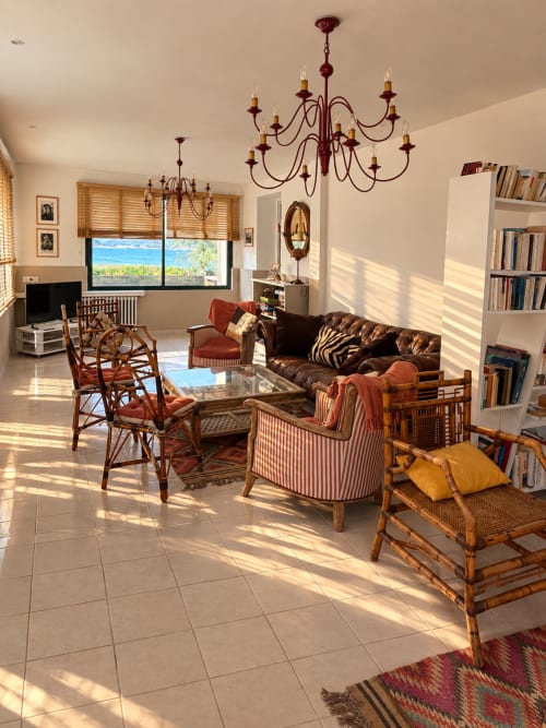 Séjour lumineux de l'Hôtel Thalassa à Cargèse avec mobilier en bois, lustre, bibliothèque et vue sur la Méditerranée