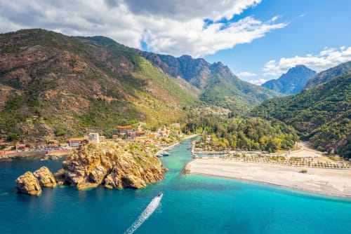 Plage méditerranéenne turquoise avec littoral rocheux, montagnes et village près de l'Hôtel Thalassa à Cargèse