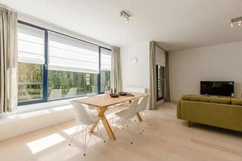 Appartement moderne à Bruxelles au Livorno avec table à manger, canapé vert et baies vitrées donnant sur la verdure