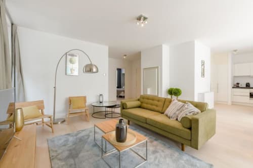 Salon moderne d'un appartement bruxellois avec canapé vert olive, chaises en bois et lampadaire arc au Livorno