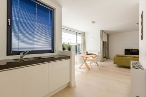 Appartement élégant à Bruxelles avec séjour ouvert, fenêtre à cadre bleu, cuisine blanche et parquet clair