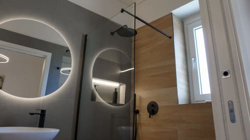 Bagno moderno presso Marelia Suites a Vasto con specchio rotondo illuminato, rubinetteria nera, doccia in vetro e dettagli in legno