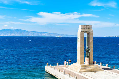 Monumento che affaccia sullo Stretto di Messina a Reggio Calabria, Italia con mare azzurro e montagne costiere