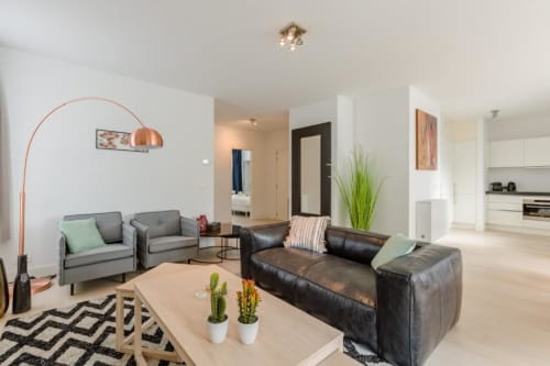 Salon moderne de l'appartement bruxellois avec sièges gris et noirs, lampadaire arc et tapis géométrique à l'hôtel Livorno