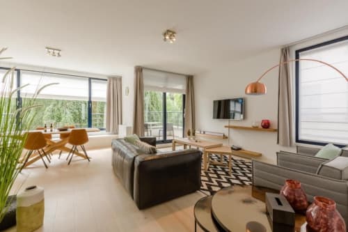 Appartement moderne et élégant à Bruxelles avec séjour ouvert, canapé noir, salle à manger, lampadaire en cuivre