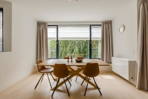 Salle à manger moderne de l'appartement Livorno Bruxelles avec table en bois, chaises beige et baies vitrées panoramiques