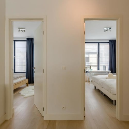 Couloir d'un appartement moderne à Bruxelles avec portes ouvertes vers deux chambres, parquet clair et design minimaliste