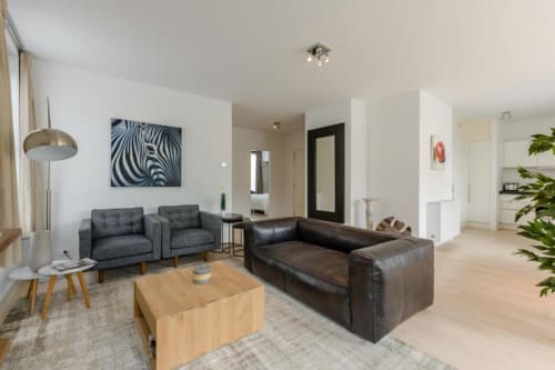 Salon moderne et élégant au Livorno Brussels avec canapé en cuir noir, fauteuils gris et table basse en bois