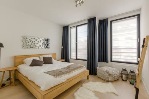 Chambre moderne et élégante de l'appartement Livorno Bruxelles avec lit en bois, rideaux gris et décoration minimaliste