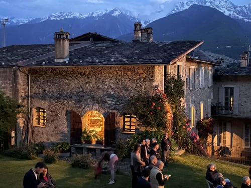 Villa in pietra a Roseto del Drago con ingresso illuminato, ospiti in terrazza giardino, montagne innevate sullo sfondo al crepuscolo