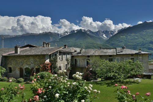 Villa in pietra con giardini fioriti che si affacciano sulle montagne innevate di Ponte in Valtellina, Italia
