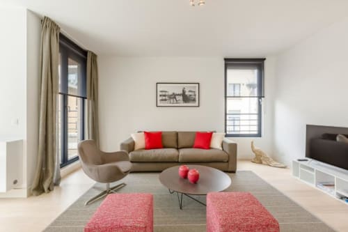 Appartement moderne à Bruxelles au Livorno avec canapé beige, accents rouges, table basse ronde et baies vitrées