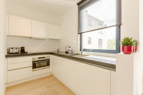 Cuisine moderne dans un élégant appartement bruxellois avec placards crème, plan de travail foncé et vue sur la ville