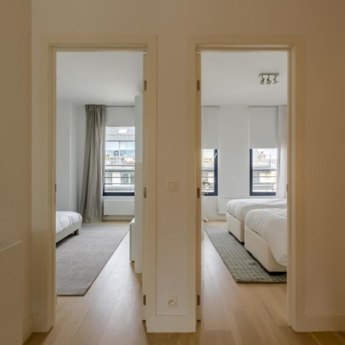 Appartement moderne à Bruxelles avec portes ouvertes révélant des chambres lumineuses, mobilier blanc, vues sur la ville et design minimaliste