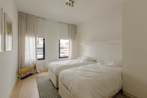 Chambre twin moderne à l'appartement The Livorno de Bruxelles, avec literie blanche, grandes fenêtres et parquet