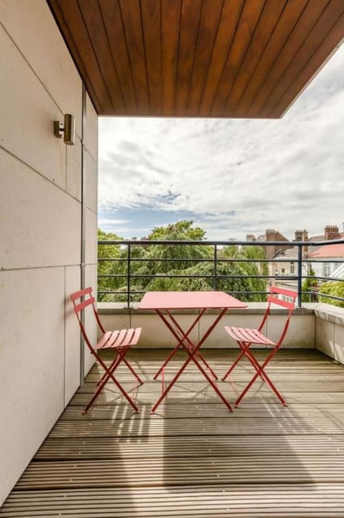 Balcon moderne du loft Livorno à Bruxelles avec chaises rouges, table rose, plafond en bois et vue sur les toits de la ville