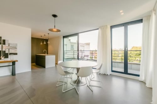 Penthouse moderne à Bruxelles avec table de salle à manger ronde, chaises blanches, cuisine ouverte et terrasse avec vue sur la ville à The