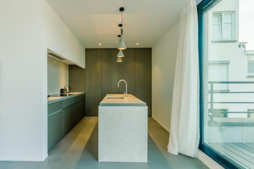 Cuisine minimaliste moderne du loft bruxellois The Livorno avec îlot blanc, placards bleu-vert et accès à la terrasse