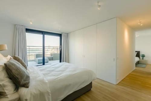 Chambre moderne dans un loft bruxellois avec lit, balcon, armoire blanche et parquet