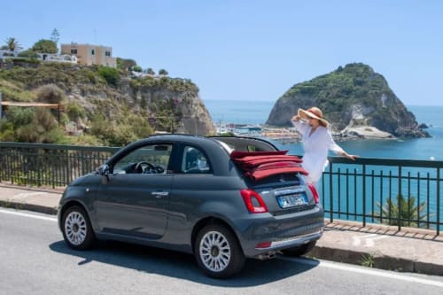 Donna con foulard rosso accanto a Fiat 500 con vista sull'Isola d'Aragonese, Serrara Fontana, Ischia