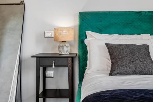 Comodino della camera da letto con lampada nell'Amor Rome Apartment, con testata teal e biancheria bianca