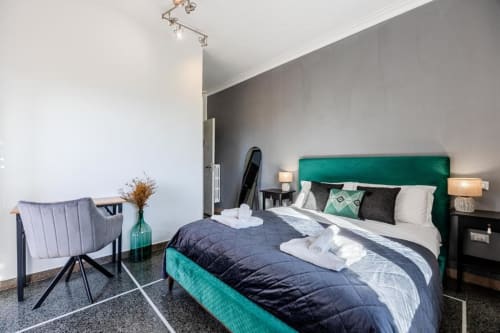 Camera da letto dell'Amor Rome Apartment con testata verde, biancheria scura, moderna poltrona e bagno privato